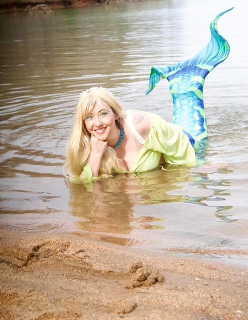 Blonde mermaid lying in the shallows with her tail fin raised